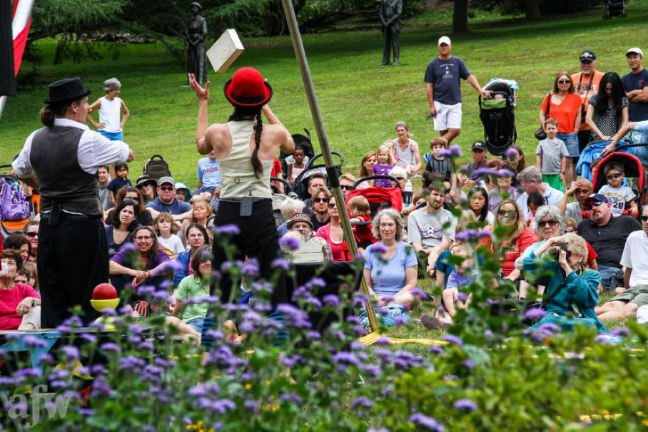 2 cigar box performers outdoors with audience 