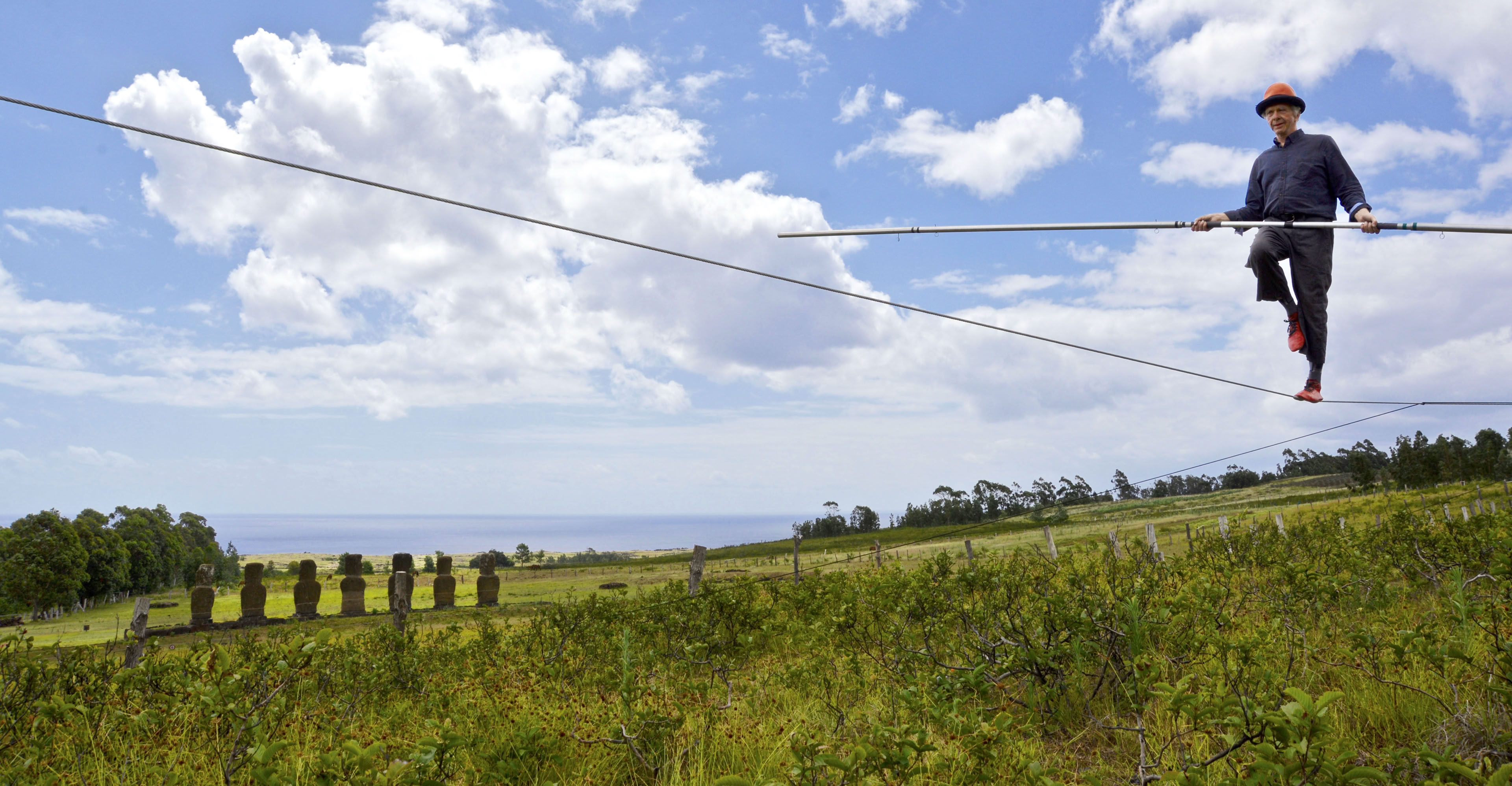 a tight wire walker with a balancing pole and moai in the background