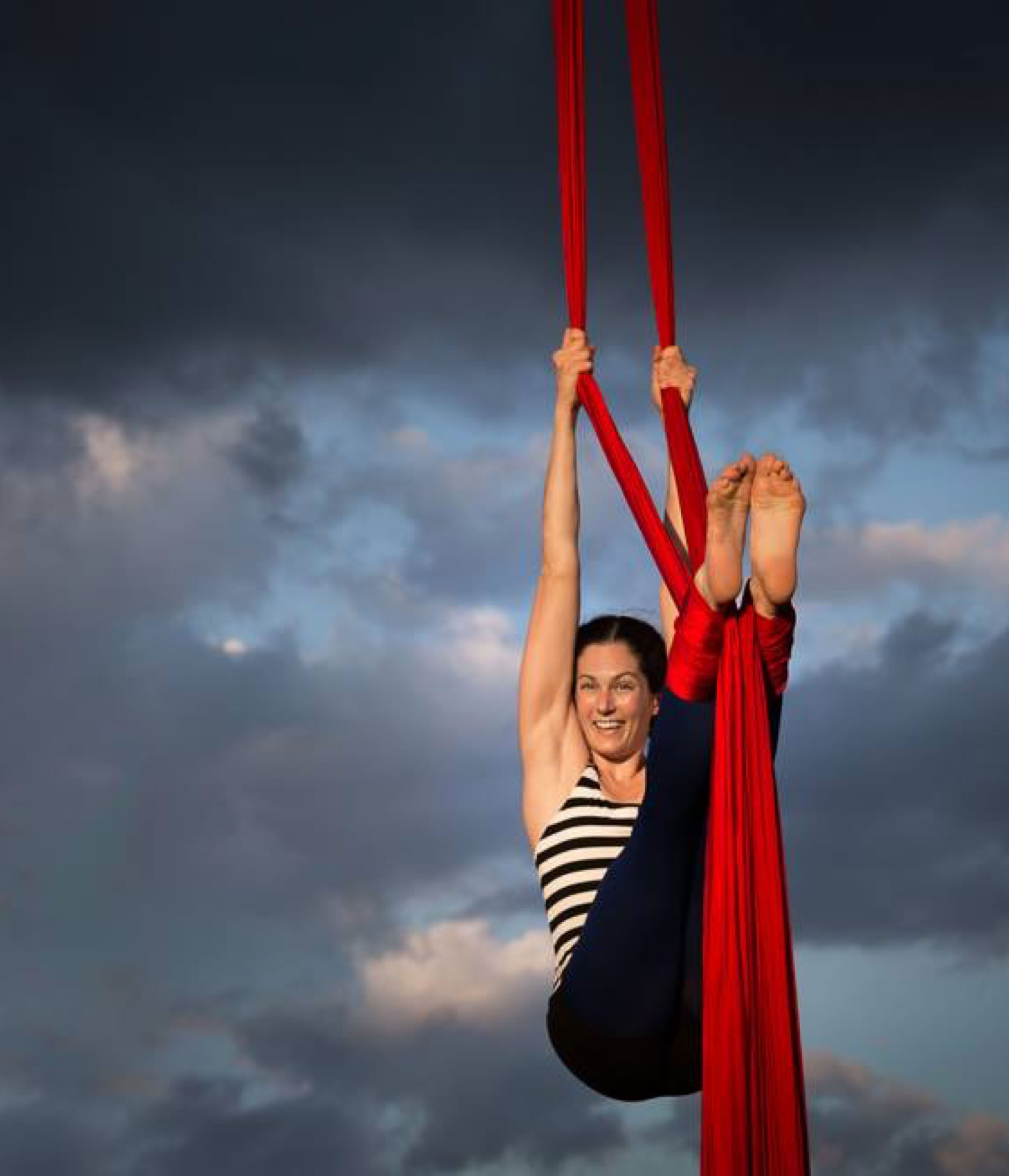 aerial silks performer outdoors against a dramatic sky